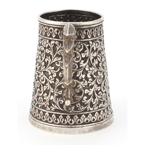 165 - Indian unmarked silver tankard of conical form, profusely embossed with flowers and foliage, 9cm hig... 