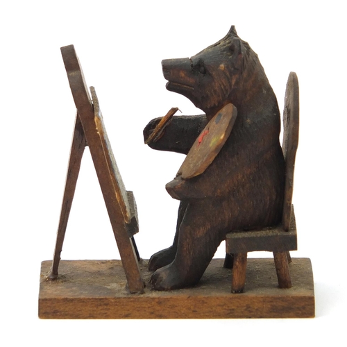 43 - Novelty miniature Black Forest carved wooden bear seated at an easel, 6cm high