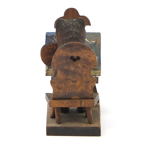43 - Novelty miniature Black Forest carved wooden bear seated at an easel, 6cm high