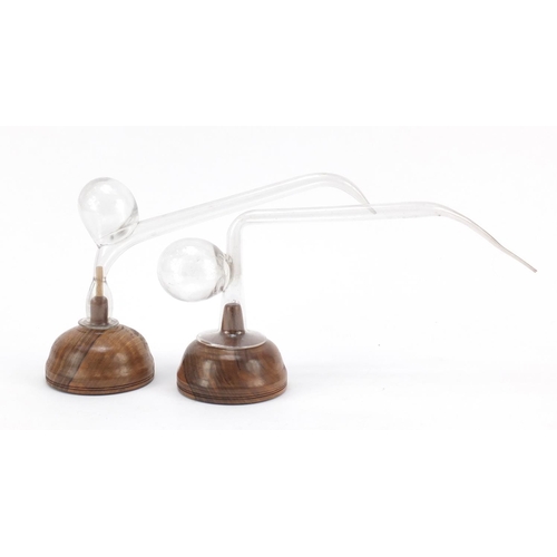 901 - Two clear glass oral breast pumps mounted on turned wooden bases, the largest 32cm in length