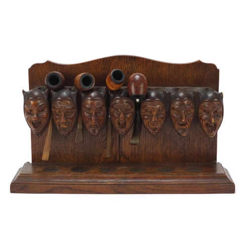 54 - Carved oak devil head design pipe stand with four pipes including two with silver mounts, the rack 3... 