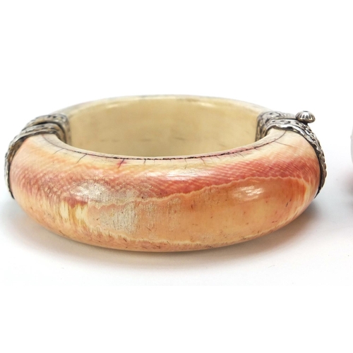 623 - Three tribal interest ivory bangles with applied silver mounts, 10cm in diameter