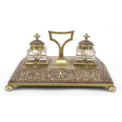 331 - 19th century copper and brass desk stand with two cut glass inkwells, the stand embossed with cherub... 