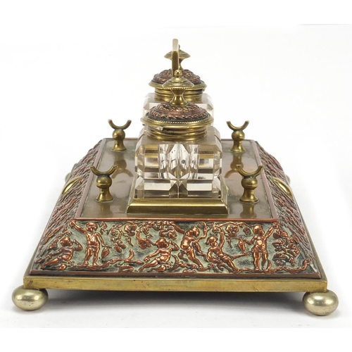 331 - 19th century copper and brass desk stand with two cut glass inkwells, the stand embossed with cherub... 