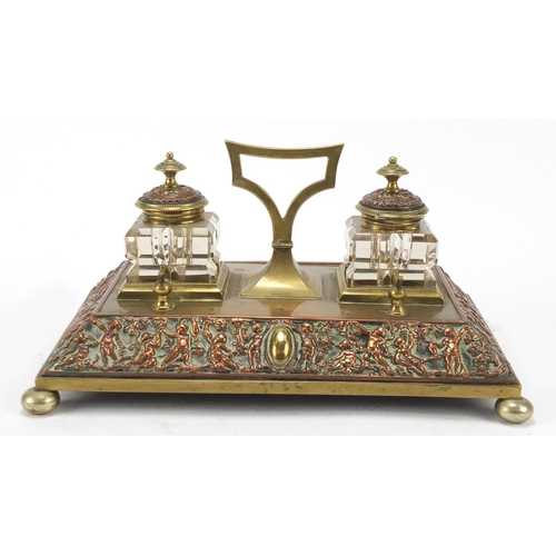 331 - 19th century copper and brass desk stand with two cut glass inkwells, the stand embossed with cherub... 