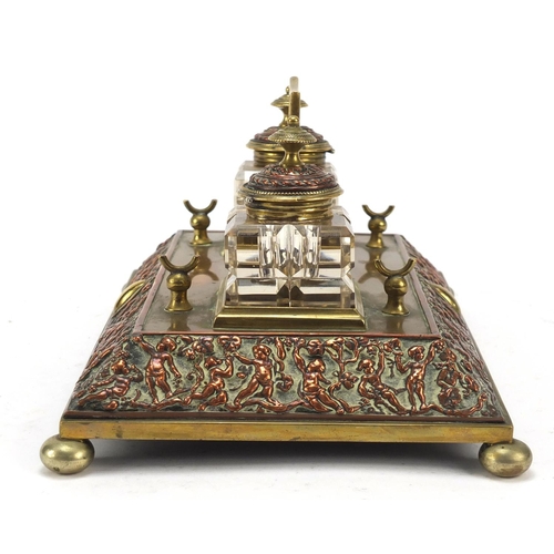 331 - 19th century copper and brass desk stand with two cut glass inkwells, the stand embossed with cherub... 