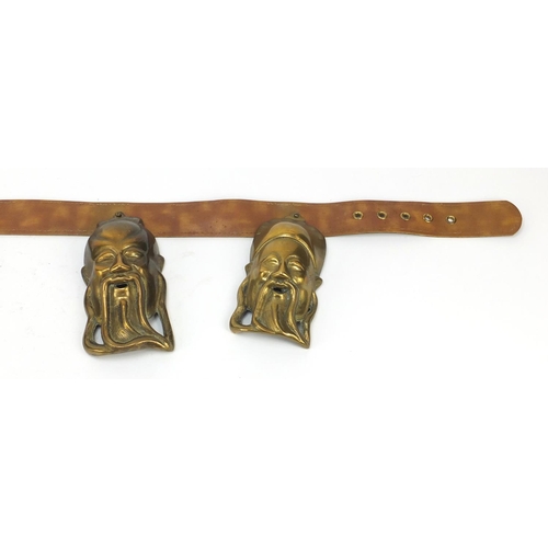 3780 - Leather belt housing four Chinese brass Emperor/Buddha heads, the largest head 16cm high