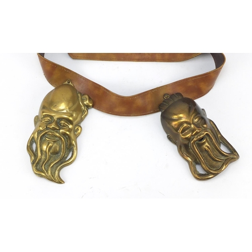 3780 - Leather belt housing four Chinese brass Emperor/Buddha heads, the largest head 16cm high