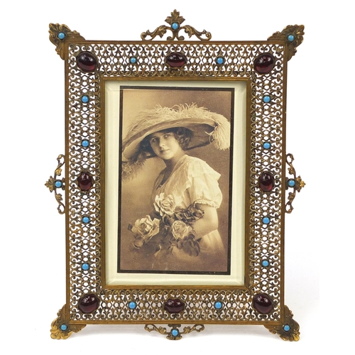 23 - Ornate pierced brass easel photo frame set with turquoise and red cabochons, 21.5cm high x 16cm wide