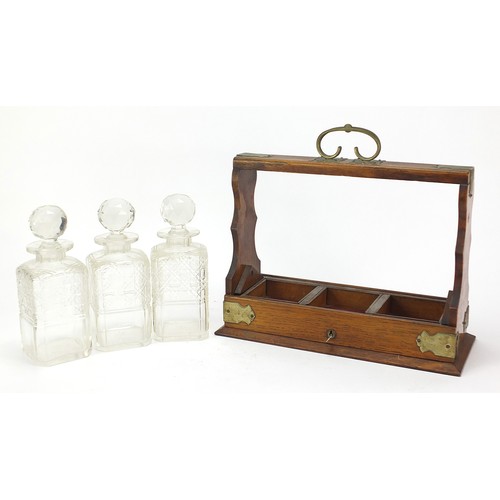 587 - Oak three bottle tantalus with three cut glass decanters and key, 32.5cm high x 36.5cm wide