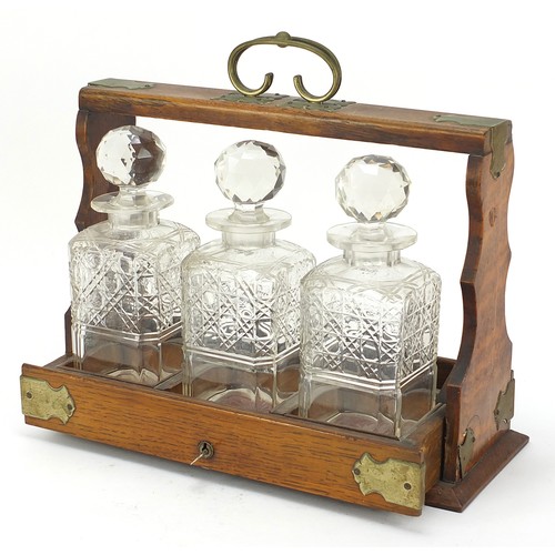 587 - Oak three bottle tantalus with three cut glass decanters and key, 32.5cm high x 36.5cm wide