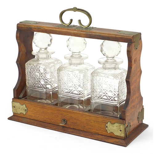 587 - Oak three bottle tantalus with three cut glass decanters and key, 32.5cm high x 36.5cm wide