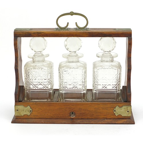 587 - Oak three bottle tantalus with three cut glass decanters and key, 32.5cm high x 36.5cm wide