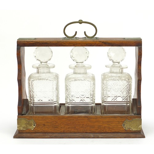 587 - Oak three bottle tantalus with three cut glass decanters and key, 32.5cm high x 36.5cm wide