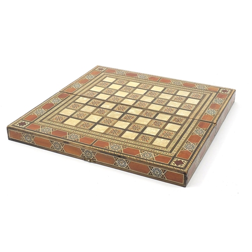 931 - Syrian Moorish design inlaid folding games/chess board with draught pieces, 49cm x 49cm when open