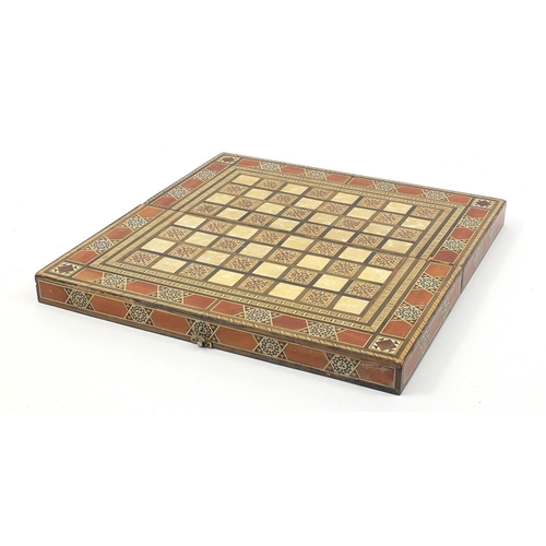 931 - Syrian Moorish design inlaid folding games/chess board with draught pieces, 49cm x 49cm when open