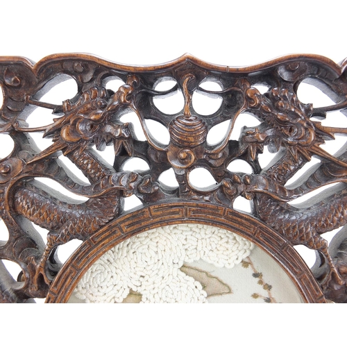 759 - Chinese hardwood frame housing an embroidered panel, the frame deeply carved with two dragons and fi... 