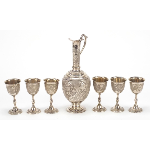 1110 - Persian silver coloured metal jug and six glasses profusely embossed and engraved with birds amongst... 