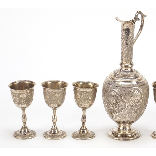 1110 - Persian silver coloured metal jug and six glasses profusely embossed and engraved with birds amongst... 