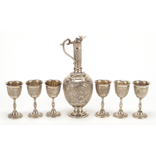 1110 - Persian silver coloured metal jug and six glasses profusely embossed and engraved with birds amongst... 