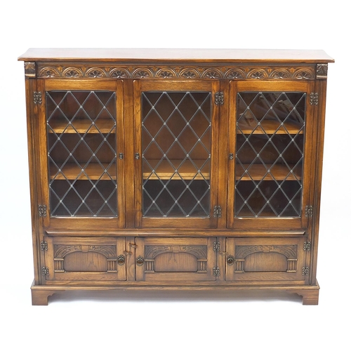 1021 - Reprodux oak bookcase fitted with three leaded glass doors encloding adjustable shelves and three cu... 