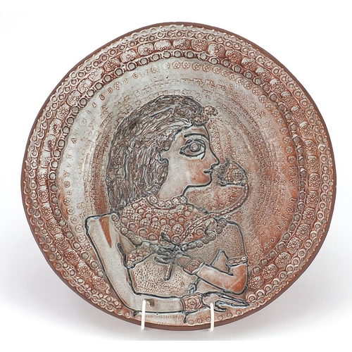 402 - Peter Askem 1964, studio pottery charger decorated in relief with a portrait of a female holding a f... 