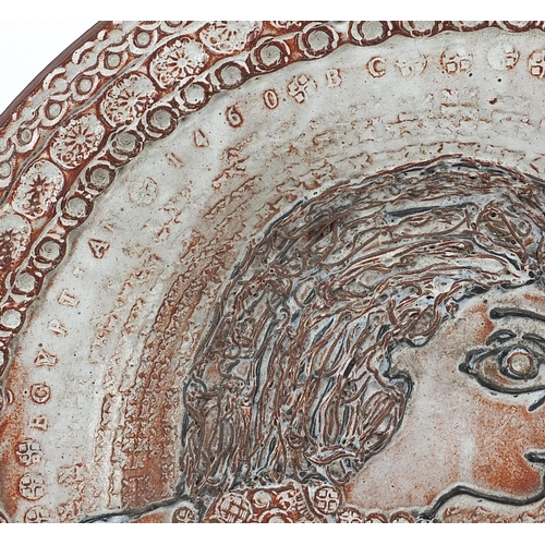 402 - Peter Askem 1964, studio pottery charger decorated in relief with a portrait of a female holding a f... 