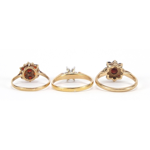 1715 - Two 9ct gold garnet cluster rings and a gold coloured metal clear stone ring, sizes K, L and M, 5.6g