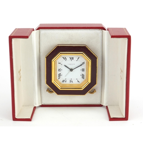 268 - Cartier red and gold coloured desk strut clock, the dial having Roman numerals, housed in a red pres... 