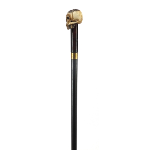 329 - Ebony walking stick with carved bone the pommel in the form of a skull, the cane 90cm in length