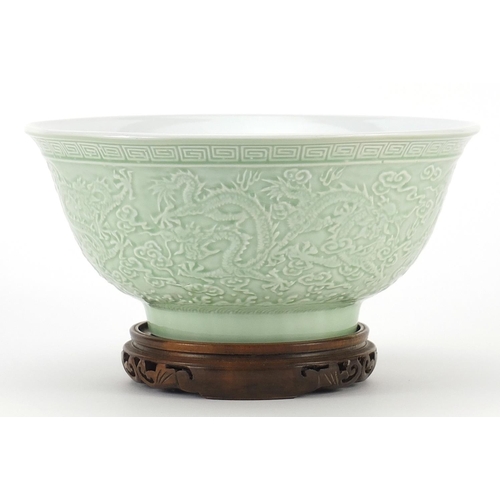 34 - Chinese porcelain bowl raised on hardwood stand having a celadon glaze, decorated in relief with dra... 