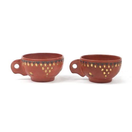 218 - Pair of Turkish tapone terracotta cups and saucers incised and gilded with flowers, each saucer 14cm... 