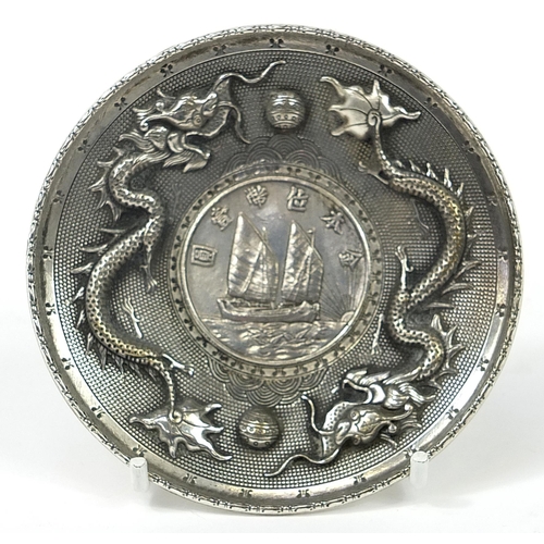 404 - Chinese silver coloured metal dragon dish inset with a boat dollar, 10cm in diameter, 105.8g