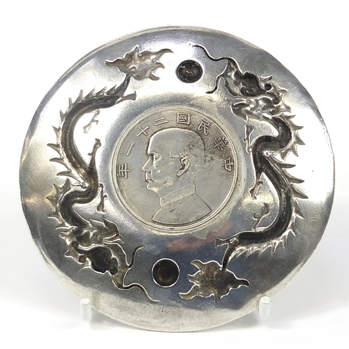 404 - Chinese silver coloured metal dragon dish inset with a boat dollar, 10cm in diameter, 105.8g