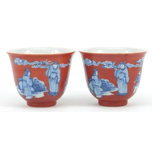 396 - Pair of Chinese iron red ground blue and white porcelain tea bowls hand painted with figures in a la... 