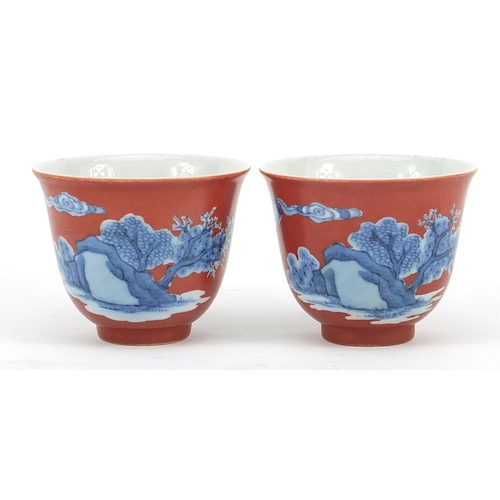 396 - Pair of Chinese iron red ground blue and white porcelain tea bowls hand painted with figures in a la... 