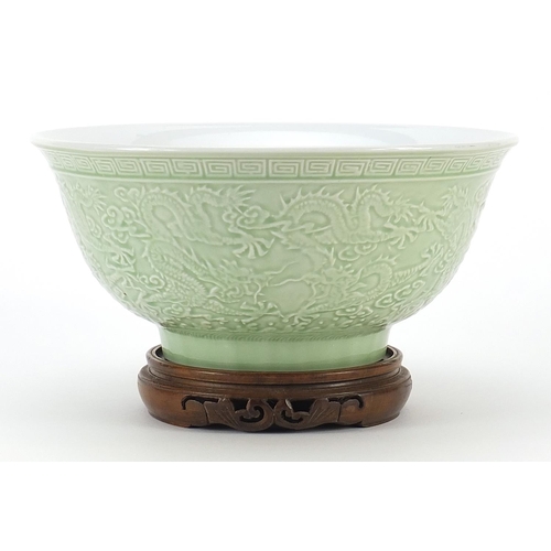 1717 - Chinese porcelain bowl raised on hardwood stand having a celadon glaze, decorated in relief with dra... 