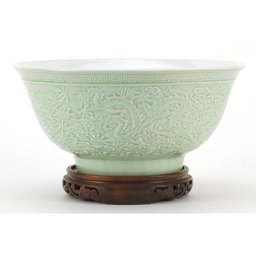 1717 - Chinese porcelain bowl raised on hardwood stand having a celadon glaze, decorated in relief with dra... 