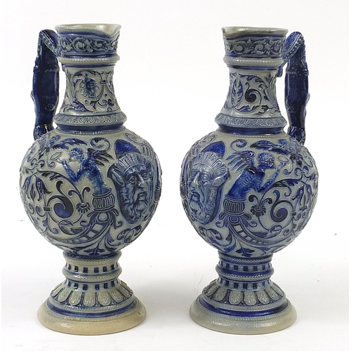 367 - Pair of German salt glazed jugs decorated with grotesque masks and foliage, 28cm high