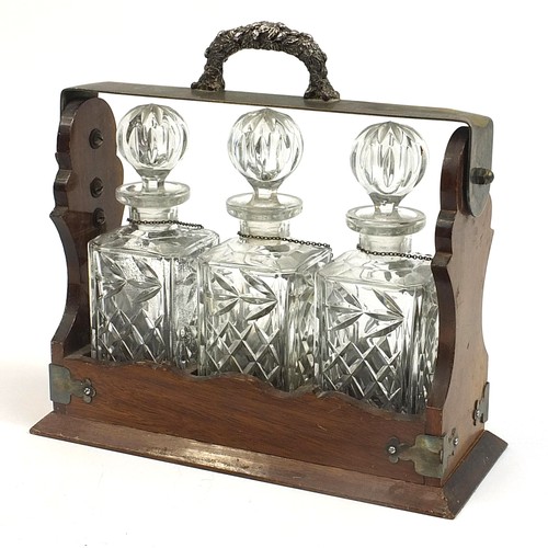 15 - Silver plated and oak three bottle tantalus with three glass decanters and three decanter labels, tw... 