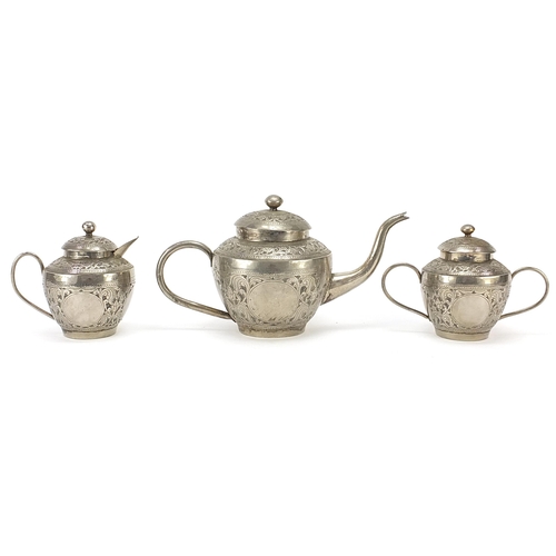 586 - Anglo Indian white metal three piece tea service embossed with flowers and foliage, the teapot 28cm ... 