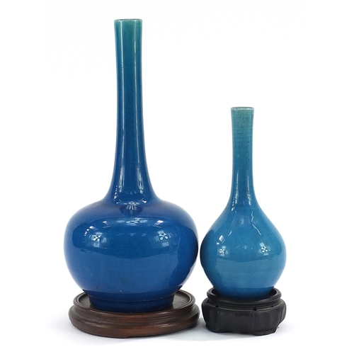 393 - Two Chinese porcelain long neck bottle vases having blue glazes raised on hardwood stands, the large... 