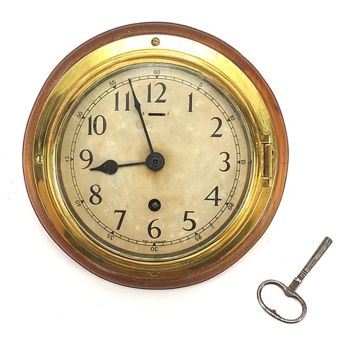 185 - Brass ship's bulkhead clock mounted on wooden back, 23cm in diameter