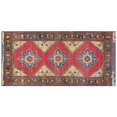 855 - Red ground rug having an all over geometric floral design, 233cm x 127cm