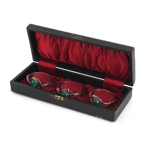 752 - Set of three white metal napkin rings set with green cabochon stones housed in a silk lined fitted b... 