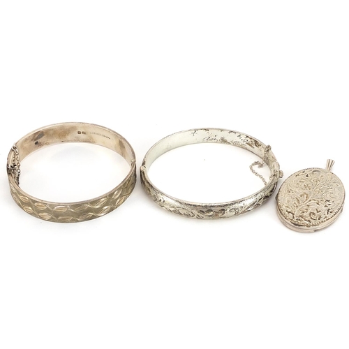 1999 - Two silver hinged bangles and a silver oval locket engraved with foliage, 62.3g