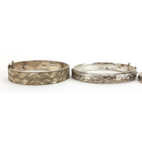 1999 - Two silver hinged bangles and a silver oval locket engraved with foliage, 62.3g