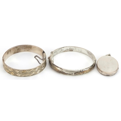 1999 - Two silver hinged bangles and a silver oval locket engraved with foliage, 62.3g