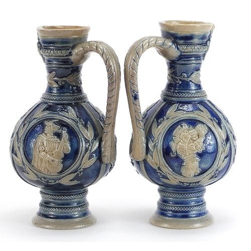 728 - Pair of German salt glazed jugs decorated in relief with classical figures, each 17.5cm high