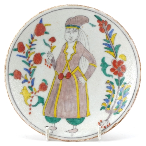 83 - Turkish Kutahya pottery dish hand painted with a figure in traditional dress and flowers, 14cm in di... 